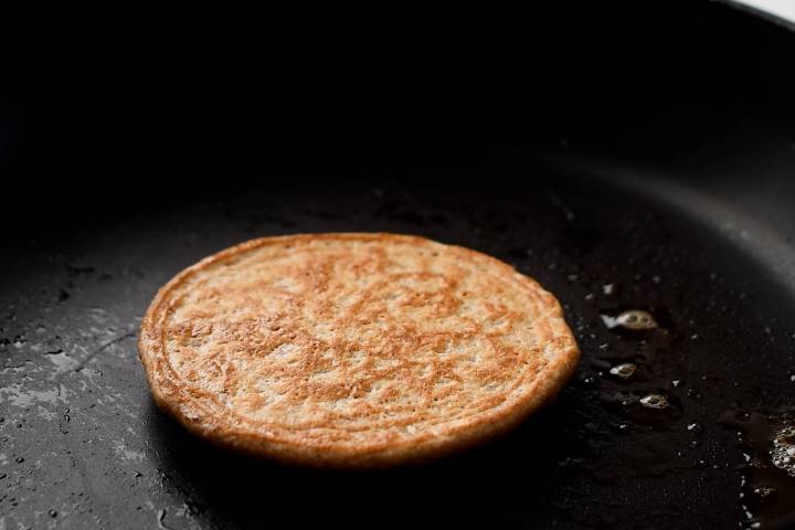 Oat pancake cooking in a hot skillet with a golden brown exterior.