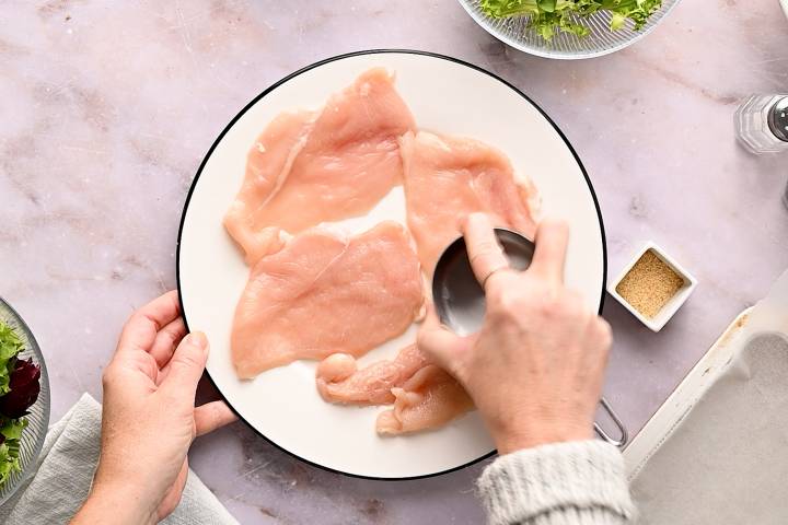 Chicken breast being pounded into uniform pieces.