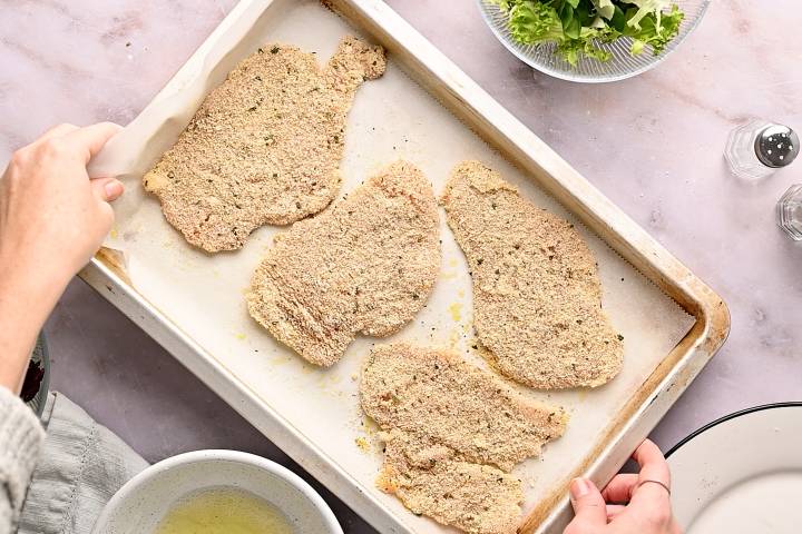 Breaded chicken cutlets on a baking sheet with parchment paper before cooking.