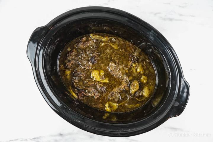 Cooked pepperoncini beef in a slow cooker with onions.