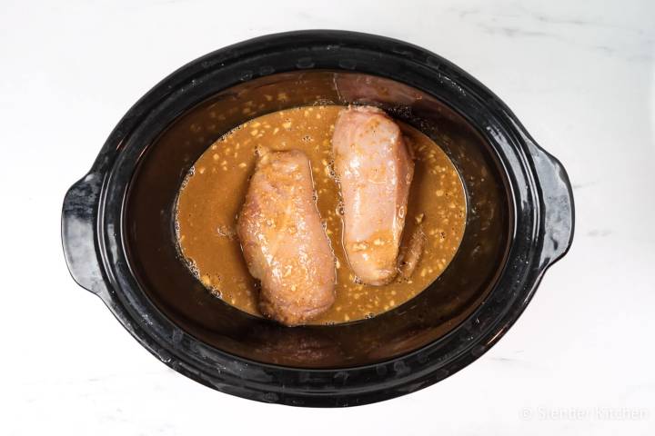 Raw chicken in a slow cooker covered with peanut sauce. 