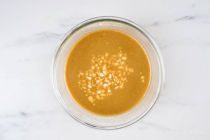 A small glass bowl with a sauce made of peanut butter, coconut milk, soy sauce, garlic, and other ingredients. 