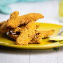 Almond chicken tenders piled on a plate with honey mustard.