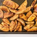 Crispy baked potato wedges on a cooking sheet with paprika, garlic powder, salt, and pepper.