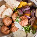 Chicken feta meatballs with fresh herbs in a bowl with tzatziki and grilled onions.