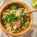 Cilantro lime cauliflower rice with fresh cilantro leaves and lime wedges in a wooden bowl.