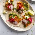 Cochinita pibil tacos with marinated shredded pork, guacamole, cilantro, pickled red onions, and limes in corn tortillas.