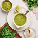 Creamy avocado salsa verde with avocados and tomatillos served in a white dish with cilantro and garlic on the side.