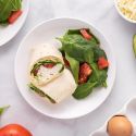 Egg white breakfast sandwich with cooked egg whites, avocado, tomatoes, spinach, and mozzarella wrapped in a tortilla.