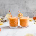 Carrot ginger smoothie with shredded carrots, banana, and mango in two glasses with straws.