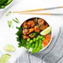 Sesame shrimp in a bowl with white rice, edamame, snow peas, and carrots.