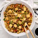 Tofu cauliflower fried rice with assorted vegetables, green onions, and soy sauce in a bowl with chopsticks.