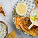 Tzatziki made with Greek yogurt, cucumbers, lemon, garlic, and dill in a bowl with pita wedges on the side.