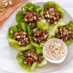 Asian ground beef lettuce wraps served on a plate with beef, mushrooms, peppers, and cashews wrapped in butter lettuce.