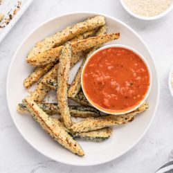 Baked Parmesan zucchini fries with a crispy panko breading on a white plate with marinara sauce.