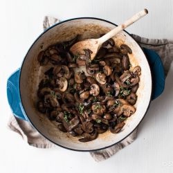 Sauteed mushrooms with garlic, butter, and thyme in a blue ceramic skillet.