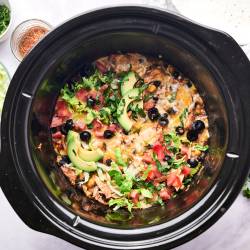 Slow cooker chicken enchilada casserole in a crockpot with avocado, black olives, lettuce, and tomatoes.