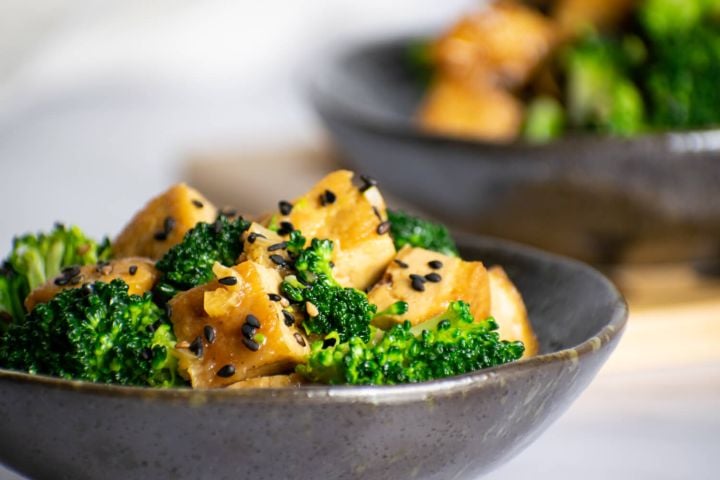Sesame tofu with broccoli and sesame seeds in a small gray bowl.