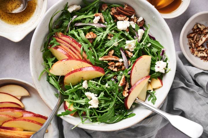 Arugula apple and goat cheese salad with pecans and lemon dressing in a bowl.