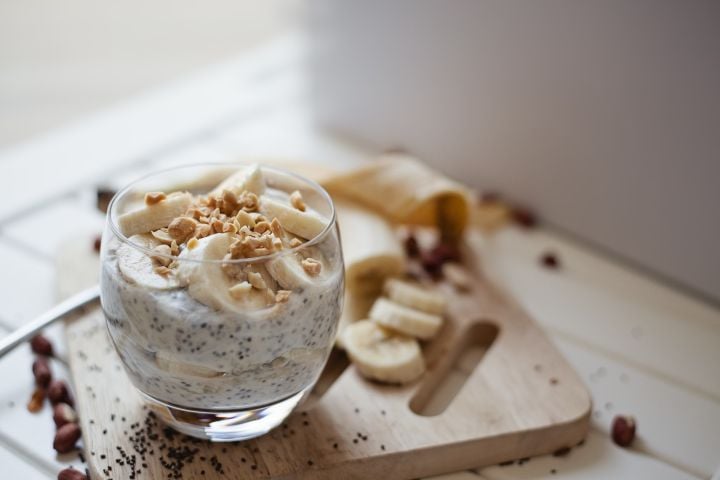 Banana chia seed pudding with almond butter served in a glass with sliced banana and cinnamon sticks. 
