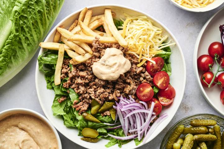 Burger bowls with seasoned ground beef, french fries, lettuce, tomatoes, red onion, pickles, and special sauce in a bowl.