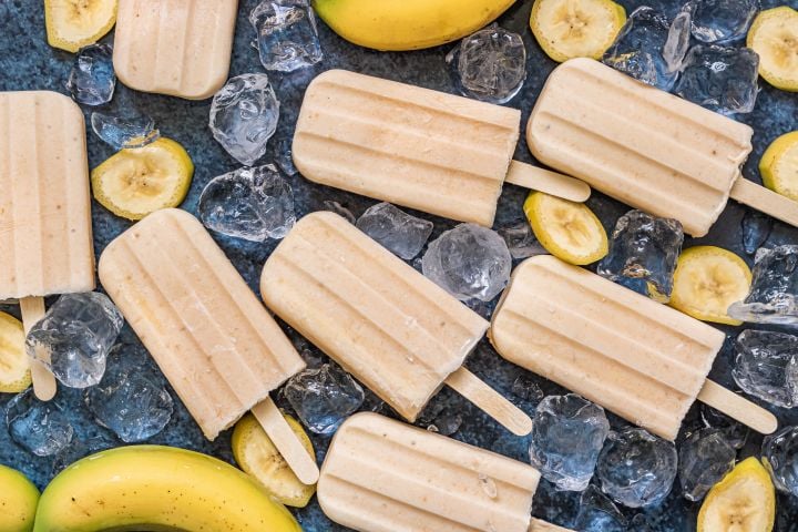 Banana popsicles with blended fresh bananas, yogurt, and honey on a marble board with banana slices. 