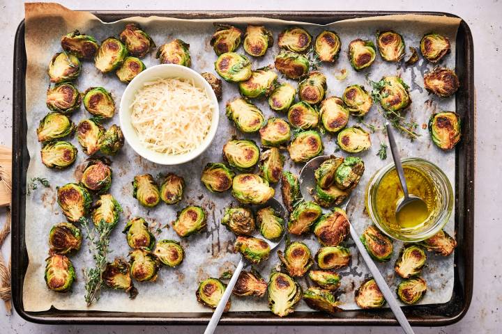 Simple roasted brussels sprouts on a baking sheet with crisp edges and Parmesan cheese.