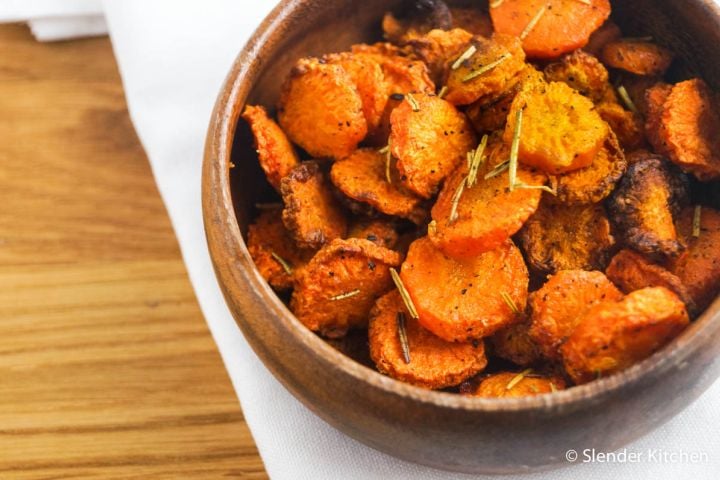 Baked carrot chips in a wooden bowl with rosemary, salt, and pepper.