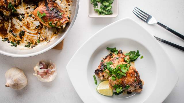 Cilantro lime chicken thighs on a plate with fresh cilantro on top and lime wedges on the side.