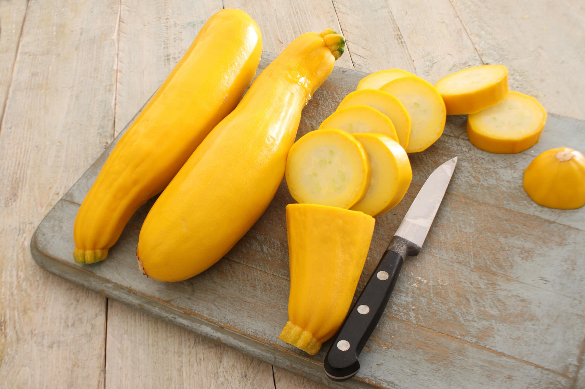 Summer squash on a cutting board with a knife.