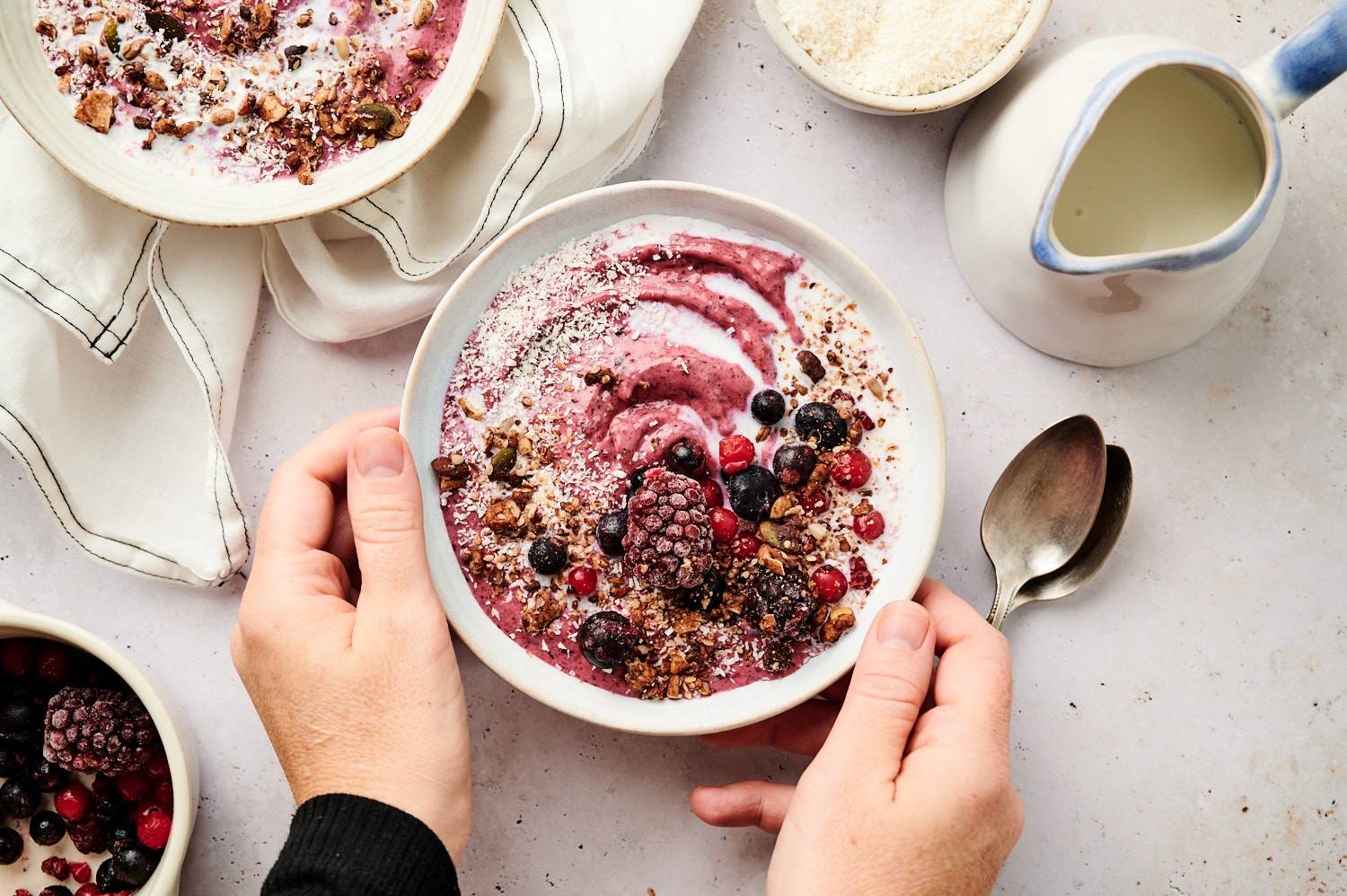 Hands holding a creamy acai bowl topped with granola, berries, and coconut.
