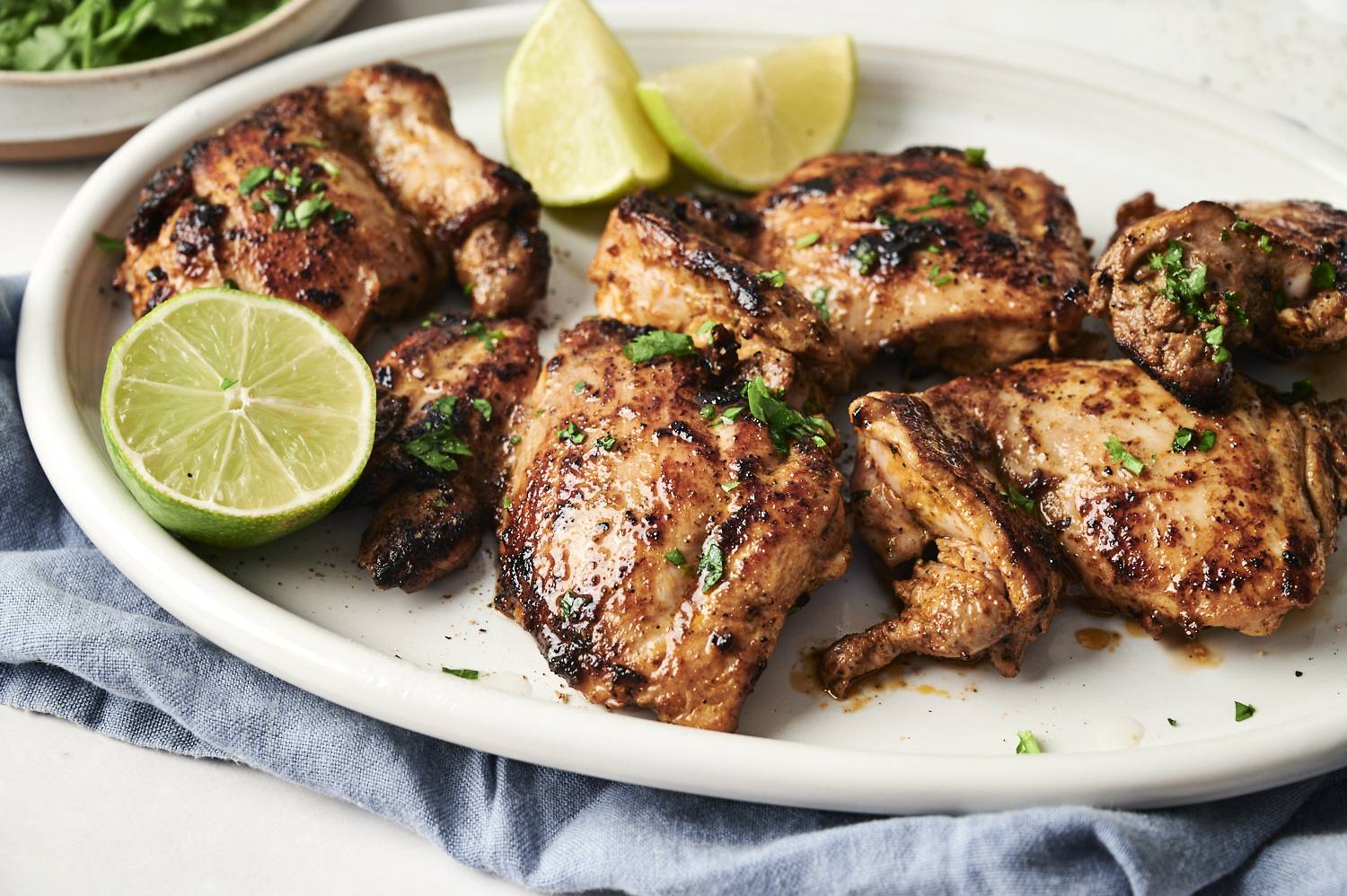Juicy grilled chipotle chicken thighs garnished with fresh cilantro and served with lime wedges on a white platter.