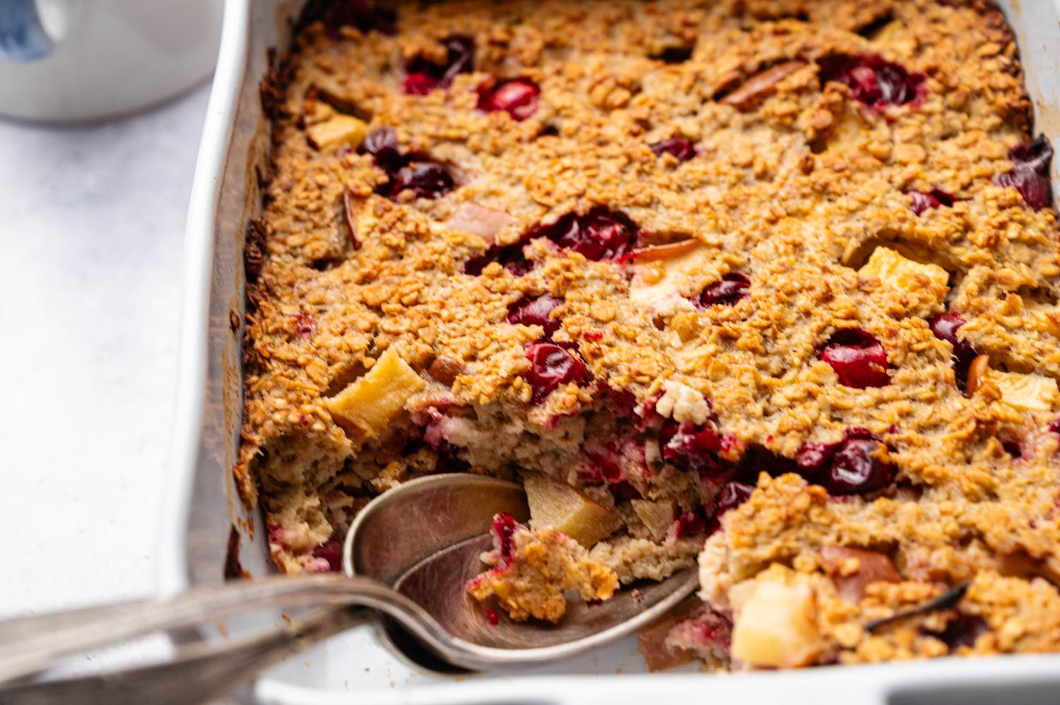 Close-up of a golden-brown baked oatmeal with cranberries and apple chunks in a dish. 