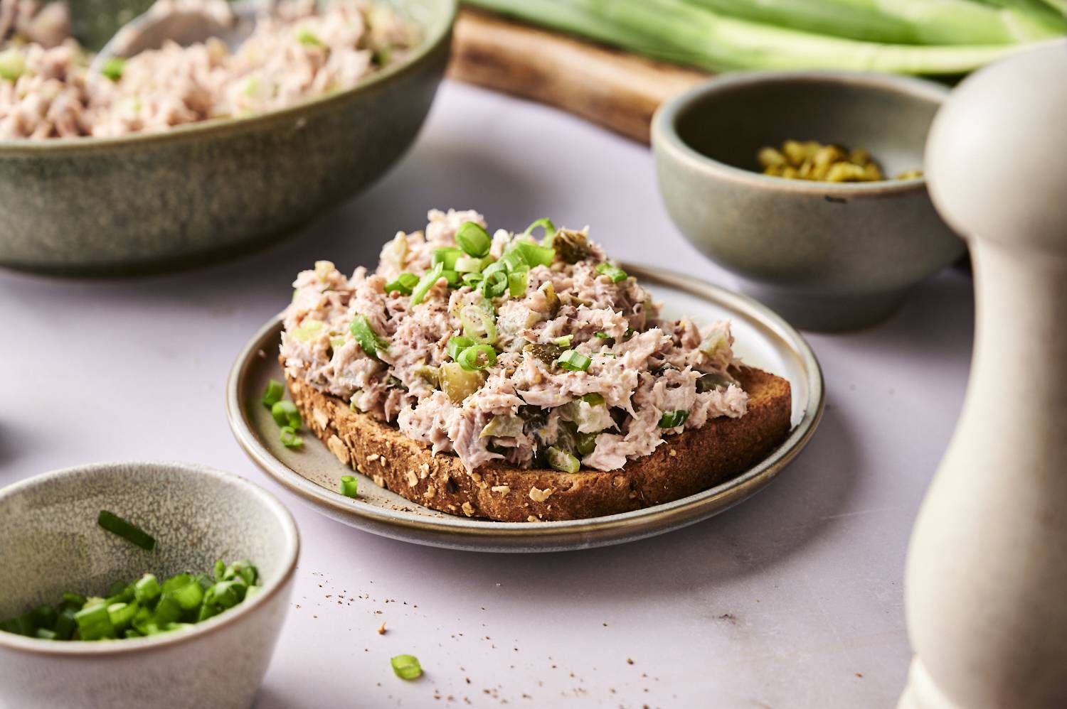 An open-faced sandwich with dill pickle tuna salad on a plate, garnished with green onions and cracked black pepper.