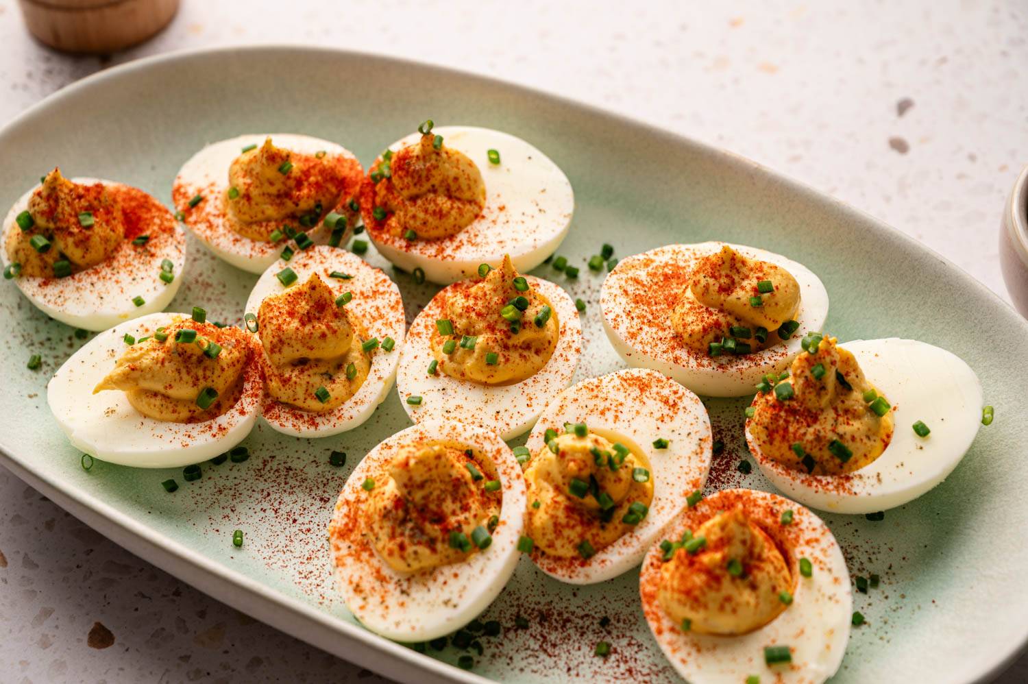 Plate of deviled eggs, garnished with paprika and chopped chives, arranged neatly on a pale green plate. 