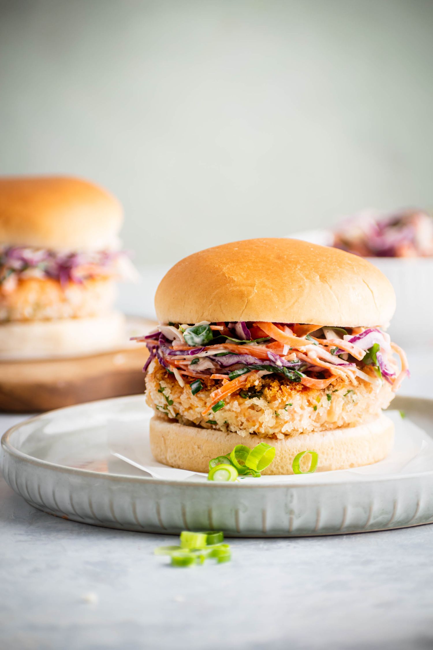 Homemade salmon burger patties served with tricolor coleslaw and green onions on a roll.