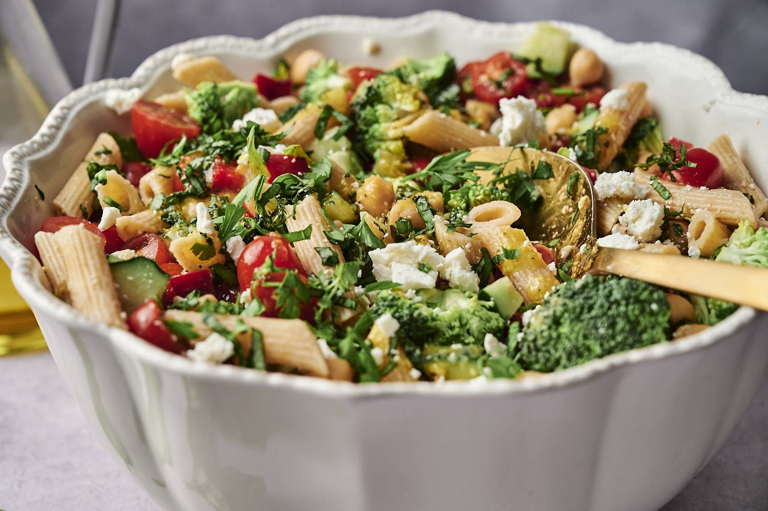 A vibrant pasta salad with penne, broccoli, cherry tomatoes, chickpeas, cucumber, and feta, garnished with fresh parsley.