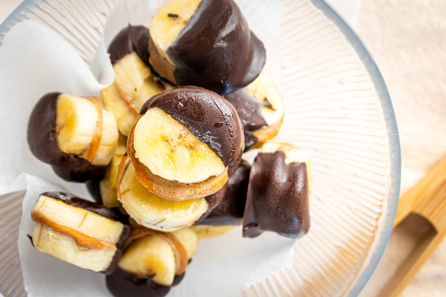 A close-up view of banana slices dipped in chocolate, arranged neatly in a bowl lined with parchment paper.