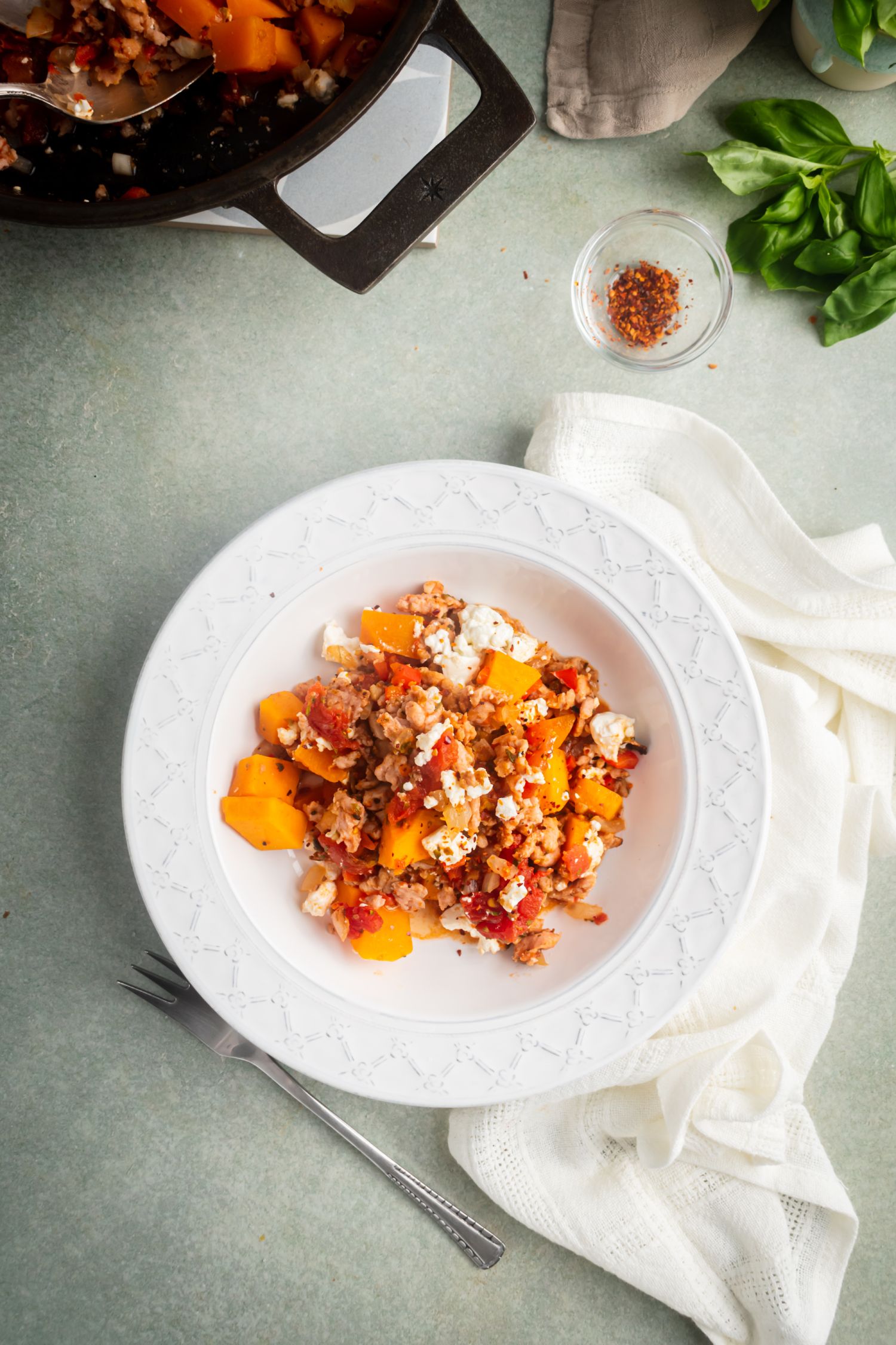 Butternut squash and ground turkey cooked with tomatoes, spices, and feta cheese in a white bowl.