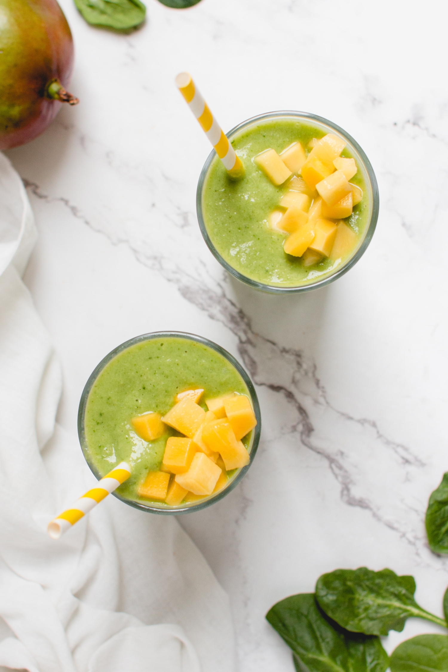 Green smoothie with mango, spinach, banana, and avocado in two glasses with mango chunks on top
