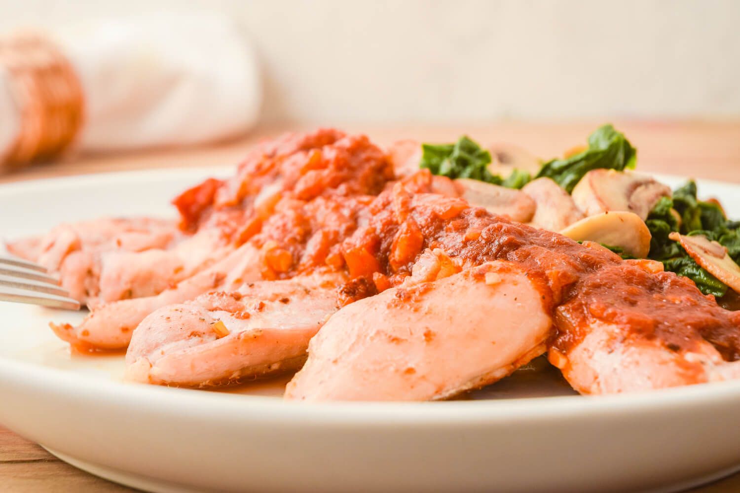 Balsamic chicken with tomatoes, mushrooms, and spinach on a white plate.