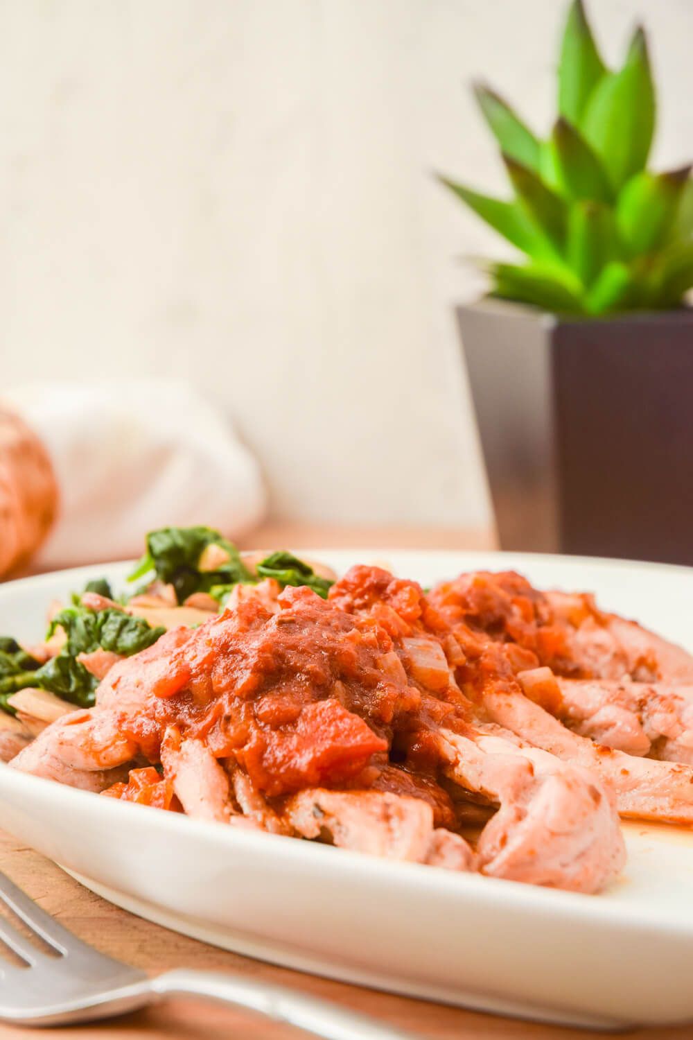 Balsamic chicken thighs with mushrooms and spinach on a plate with diced tomatoes.