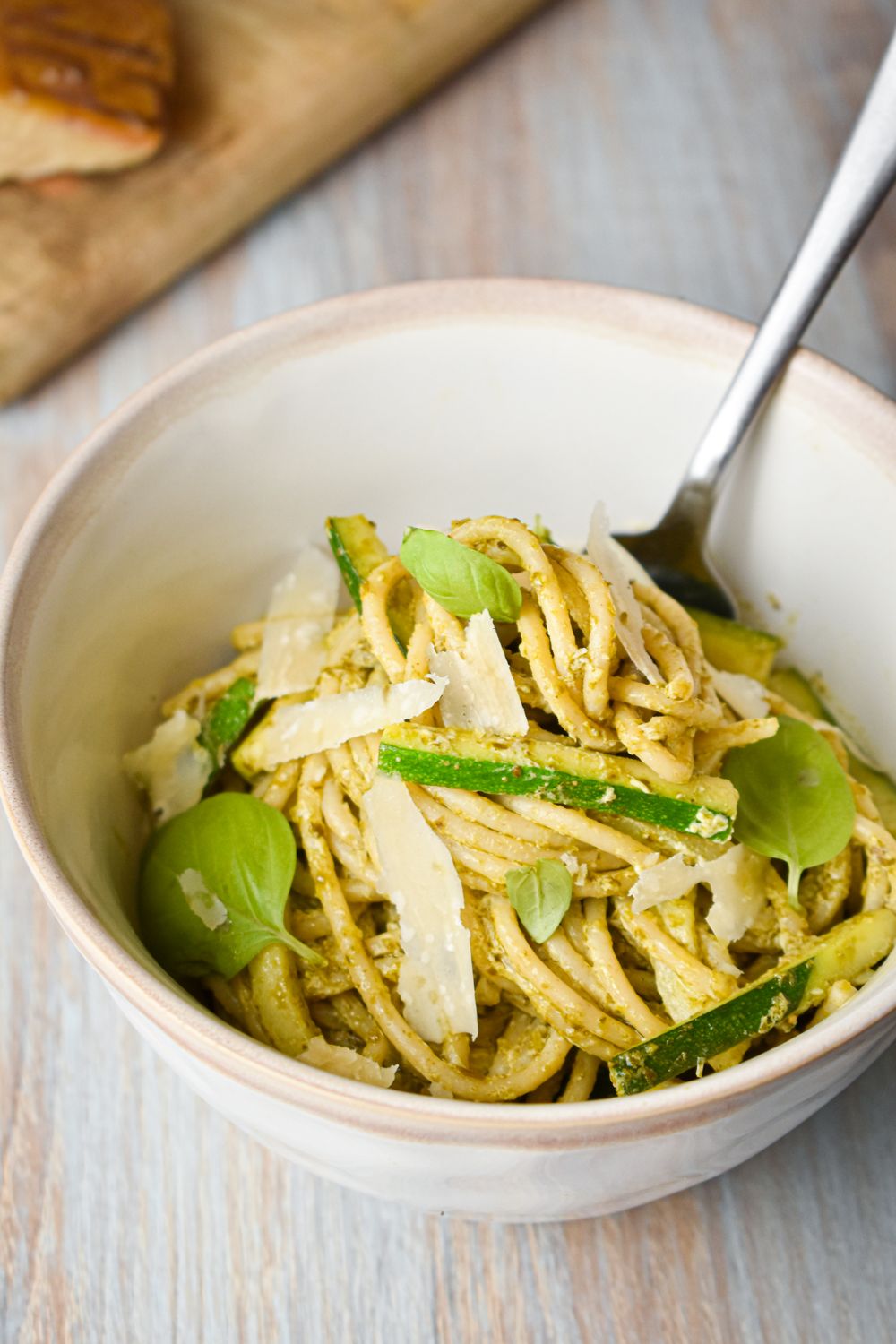 Pesto pasta with zucchini and fresh Parmesan cheese in a bowl with a fork.