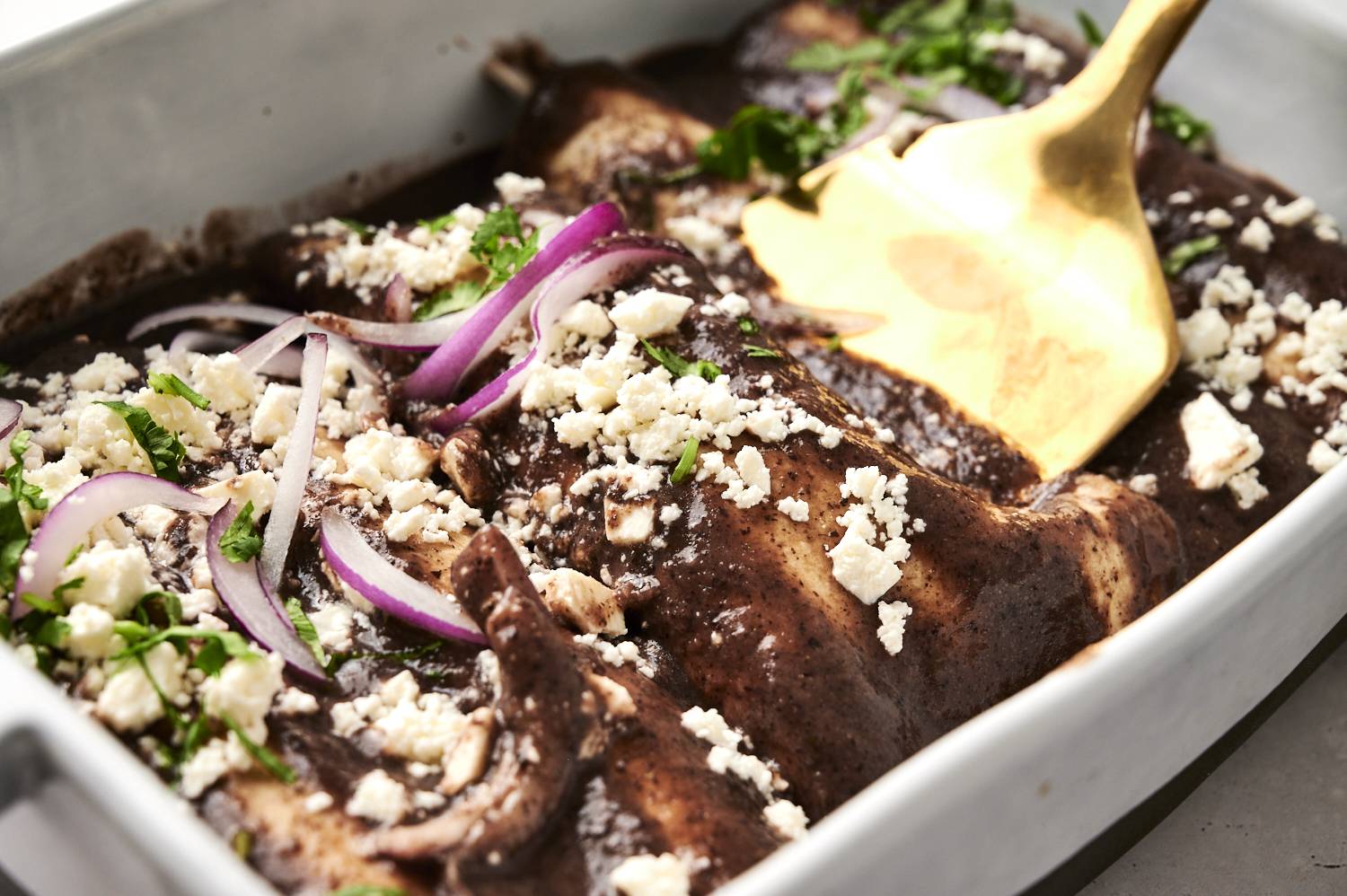 A spatula pulling up an Enfrijolada out of the pan.