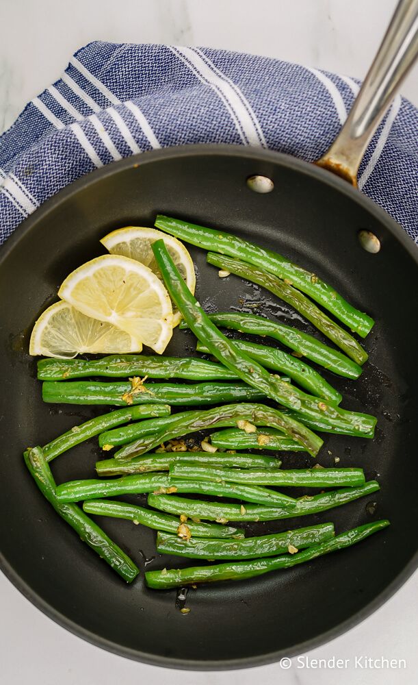 Green beans with garlic in a pan with lemon slices on a blue napkin.