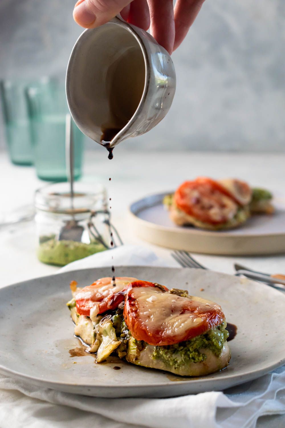 Pesto chicken with tomatoes, and melted mozzarella cheese with balsamic vinegar being drizzled on top.
