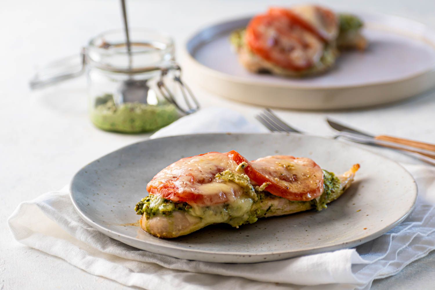 Pesto Chicken breast baked with sliced tomatoes and mozzarella cheese on a plate.