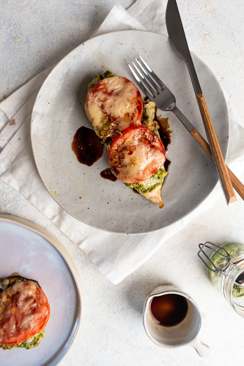 Baked chicken with pesto, tomatoes, and mozzarella cheese on top on a plate with a white napkin.