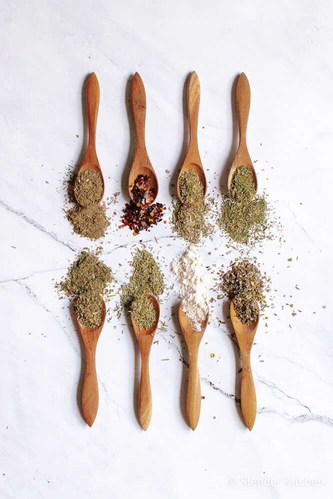 Dried herbs and spices on wooden spoons to make homemade Italian seasoning.