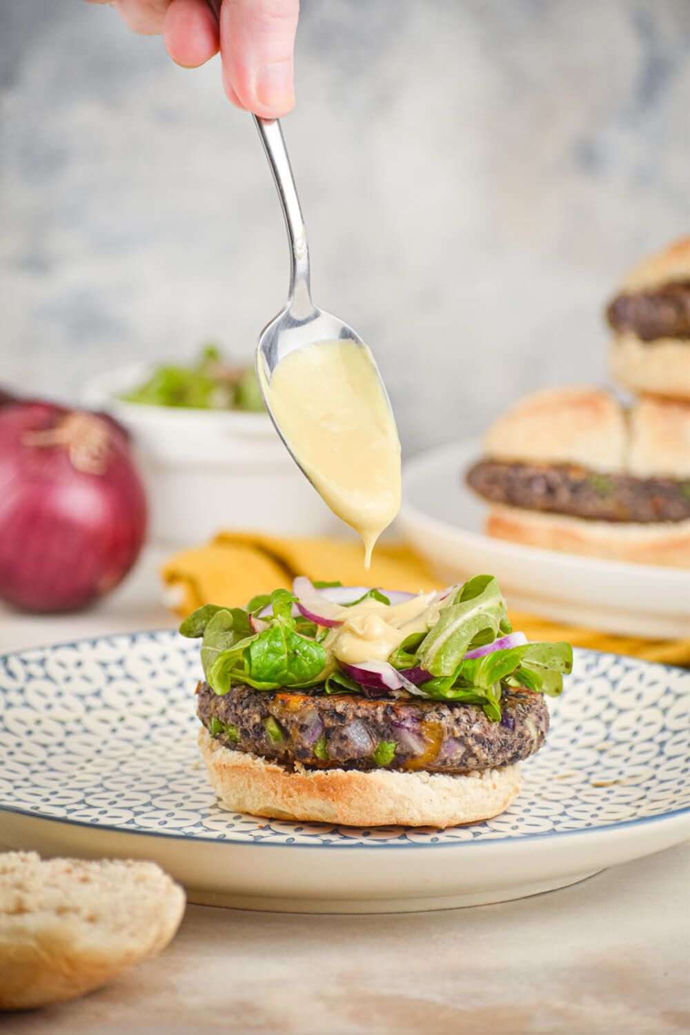 Vegetarian jalapeno cheddar black bean burgers with honey mustard sauce being dripped on top by a spoon.